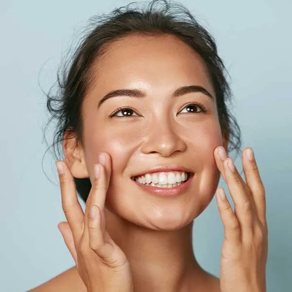 Woman smiling as she applies skin products to her face